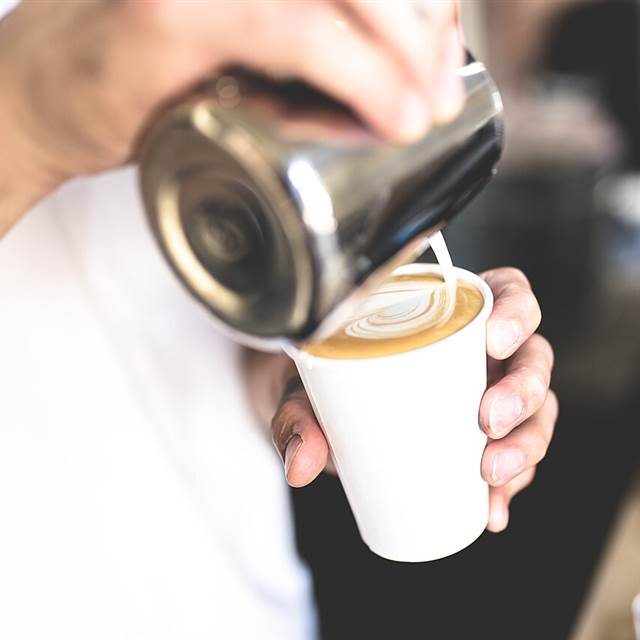 Milk being poured into a latte in a paper cup